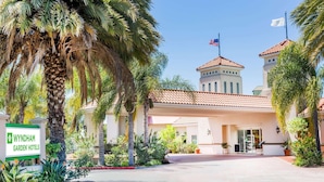 A hotel entrance with a sign, palm trees, and a building with a tiled roof. - Uptown Oasis San Jose Airport (San Jose)