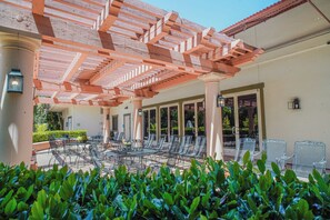 An outdoor seating area with metal chairs and tables, a pergola structure, and a garden with green foliage. - Uptown Oasis San Jose Airport (San Jose)