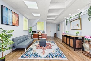 A modern living room with a grey sofa, a patterned rug, a wooden desk, and a large painting on the wall. - Econo Lodge Montgomery South I-65 (Montgomery)