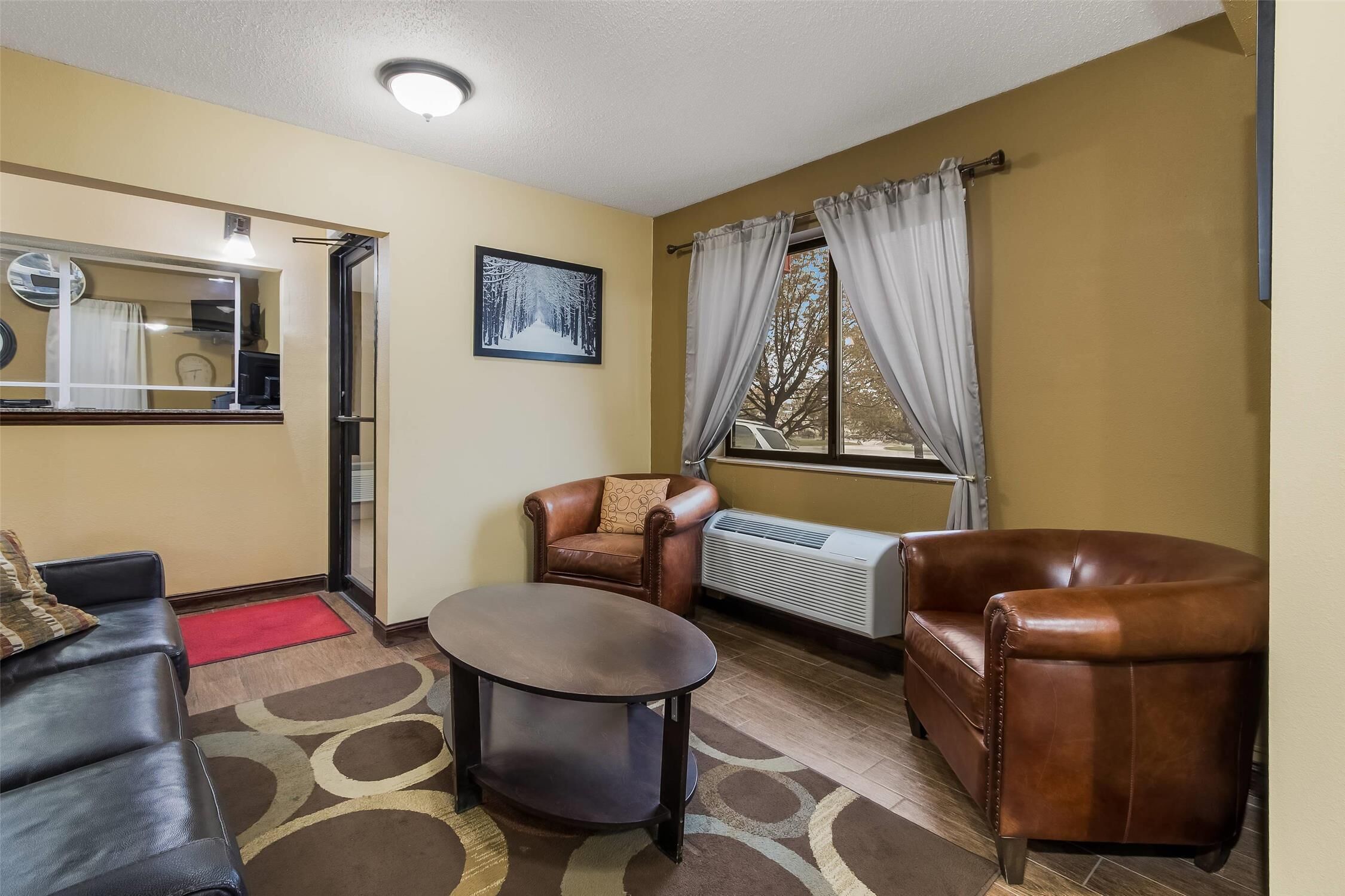 A living room with a brown leather sofa, a smaller brown leather armchair, a round coffee table, and a radiator.