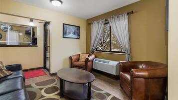 A living room with a brown leather sofa, a smaller brown leather armchair, a round coffee table, and a radiator.