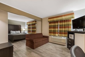 A hotel room with a bed, a sofa, a TV, a desk with a computer, and a mirror. - Econo Lodge Inn & Suites Yankton, SD (Yankton)