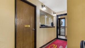 Un pasillo de hotel con una puerta de madera, una recepción y una alfombra roja con un logotipo.