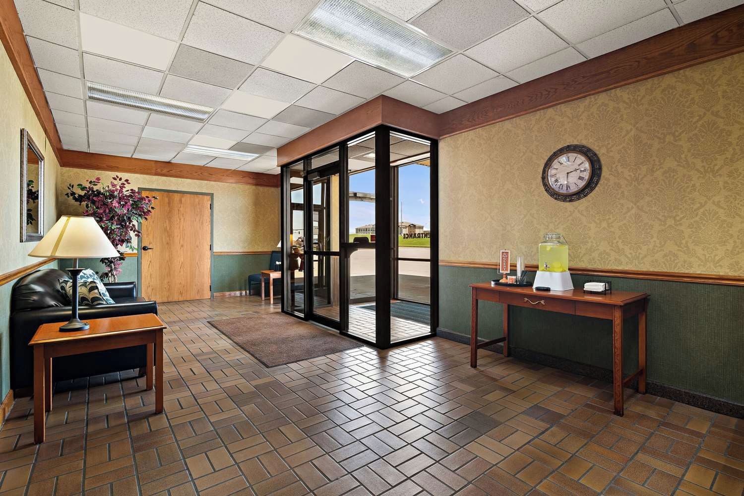 A hotel lobby with a reception desk, a seating area, a clock on the wall, and a view through a glass door.