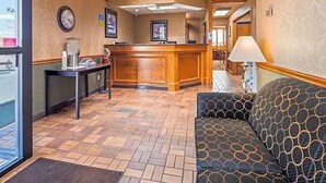 Um saguão de hotel com balcão de recepção, relógio, máquina de café e um sofá estampado.