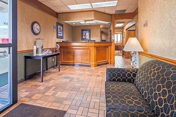 Eine Hotelhalle mit einer Rezeption, einer Uhr, einer Kaffeemaschine und einem gemusterten Sofa.