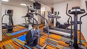 Een hotelgym met diverse fitnessapparaten, waaronder loopbanden, elliptische trainers en een hometrainer.