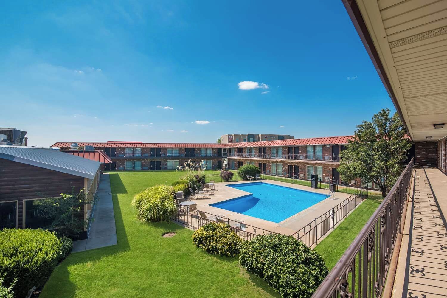 A hotel with a swimming pool, outdoor seating, and a well-maintained lawn.