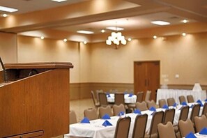 A conference room with a podium, tables with blue tablecloths, and chairs. - Rodeway Inn Mcpherson East (McPherson)