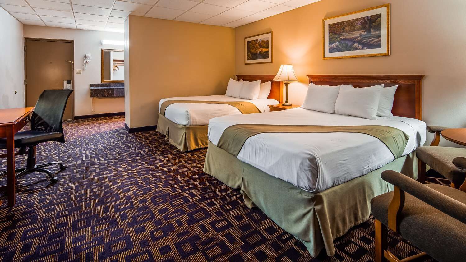 Une chambre d’hôtel avec deux lits, un bureau, une chaise, une lampe et un tableau au mur.