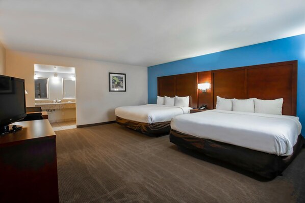 A hotel room with two beds, a desk with a TV, a bathroom with a mirror, and a framed picture on the wall. - Motel6 Willcox, AZ (Willcox)