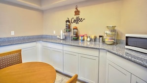 A kitchen with white cabinets, a granite countertop, and a coffee-themed wall decoration. - Motel6 Willcox, AZ (Willcox)