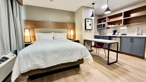 A hotel room with a bed, bedside lamps, a desk with a chair, a microwave, and a small kitchenette.