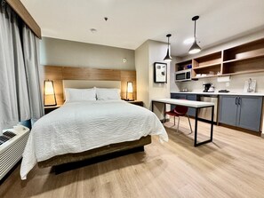 Hotellihuone, jossa on sänky, yöpöytävalaisimet, työpöytä tuolilla, mikroaaltouuni ja pieni keittokomero.