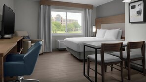 A hotel room with a bed, desk, chair, and a large window with curtains.