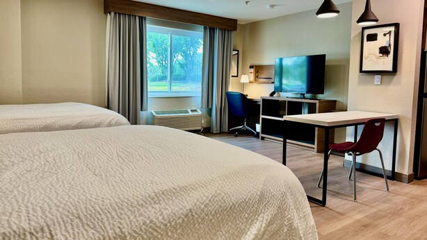 A hotel room with two beds, a desk, a chair, a TV, and a window with curtains.