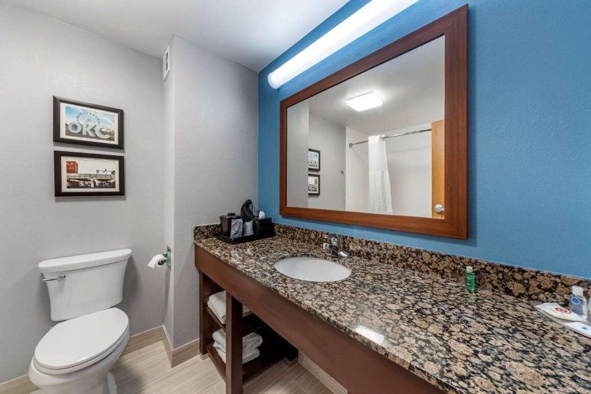 Une salle de bain avec des toilettes blanches, un lavabo surmonté d’un plan de travail en granit et un grand miroir.