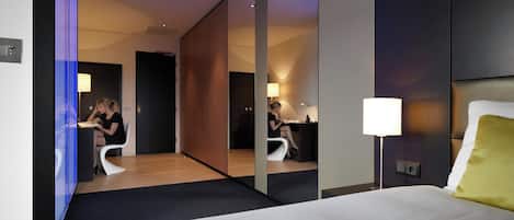 A modern hotel room with a large bed, a desk, and a mirror.