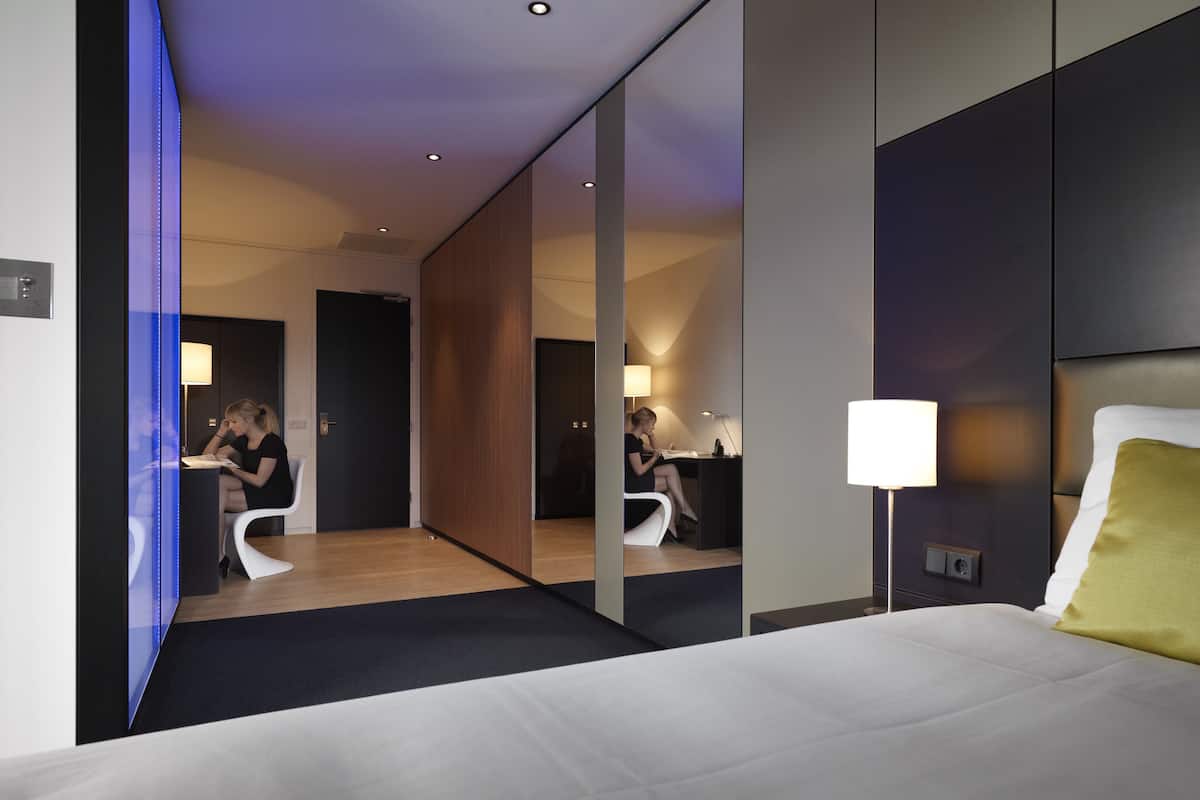 Ein modernes Hotelzimmer mit einem großen Bett, einem Schreibtisch und einem Spiegel, der den Raum widerspiegelt.