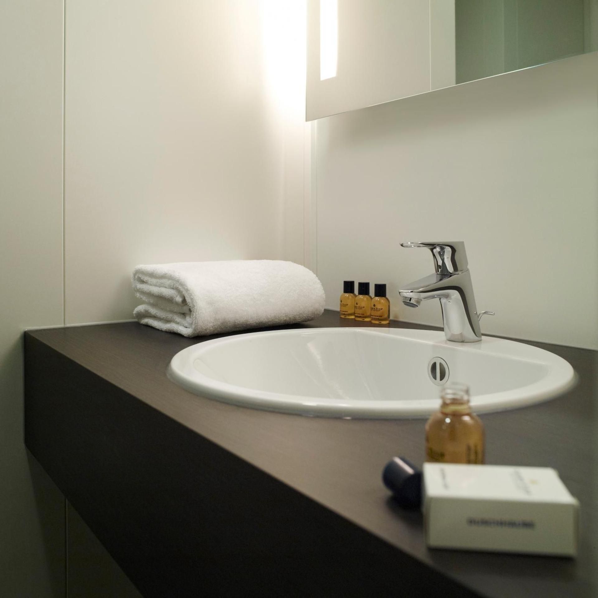 A modern bathroom with a white sink, a towel, and toiletries.