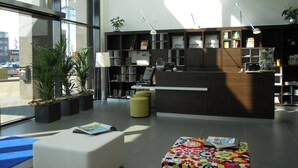 Una moderna zona de recepción con mostrador, asientos, plantas en macetas y una estantería.
