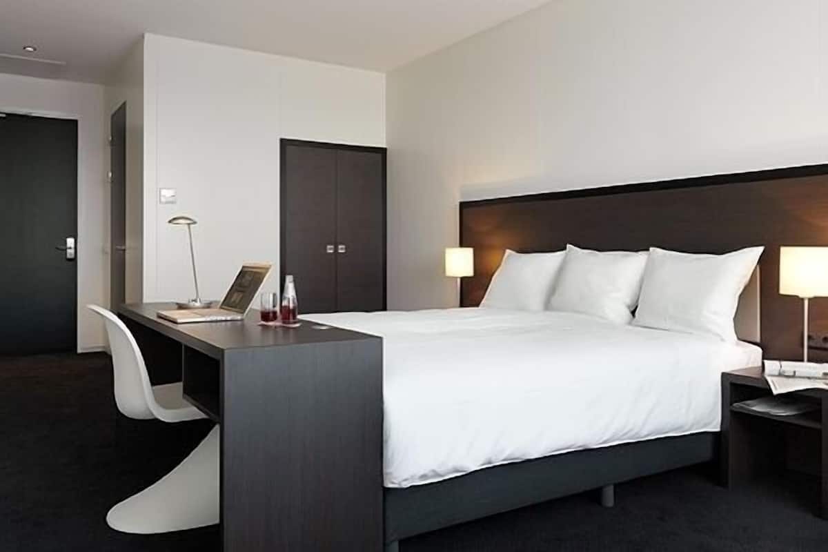 Ein modernes Hotelzimmer mit Bett, Schreibtisch, Stuhl und zwei Nachttischlampen.