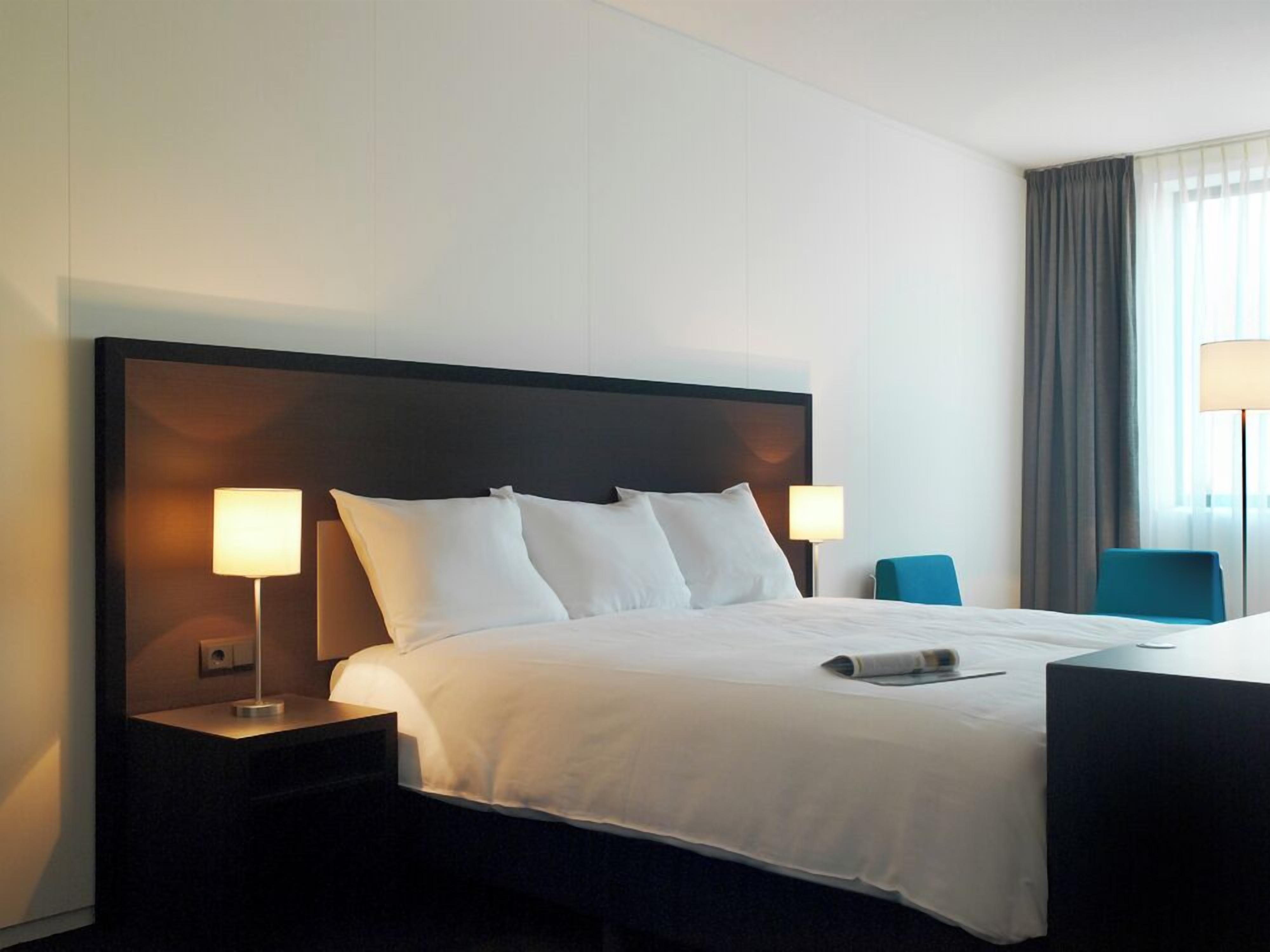 Een hotelkamer met een groot bed, twee bedlampen, een nachtkastje, een bureau en een stoel.