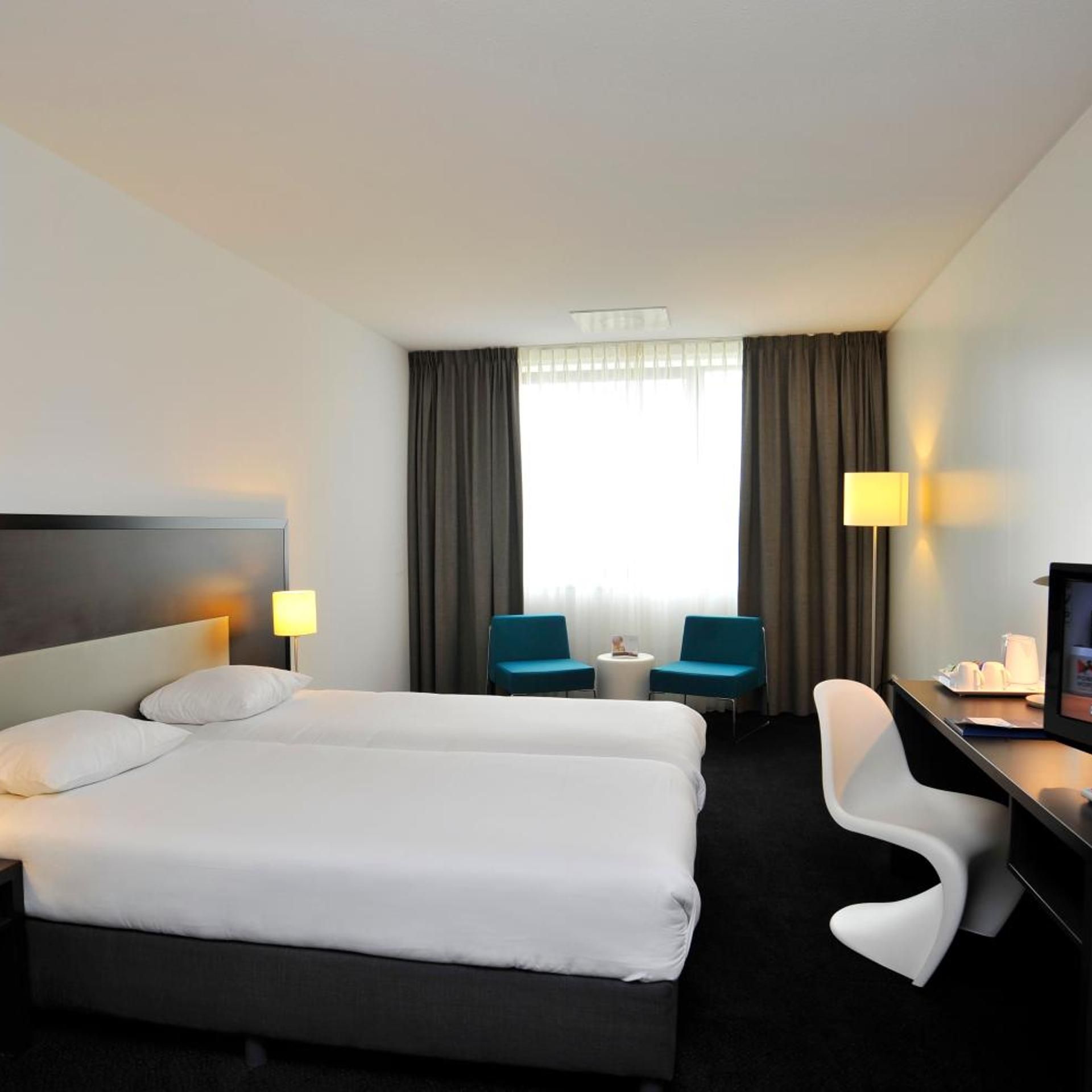 Ein Hotelzimmer mit Doppelbett, zwei Sessel, einem Schreibtisch und einem Fernseher.
