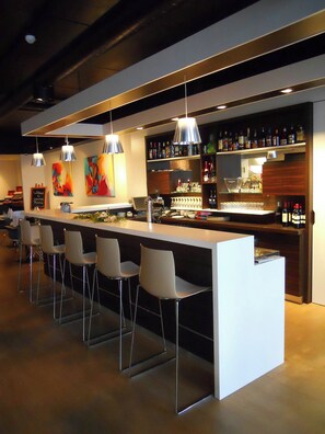 Un bar moderne doté d’un long comptoir, de nombreux tabourets, de luminaires suspendus et d’étagères remplies de bouteilles.