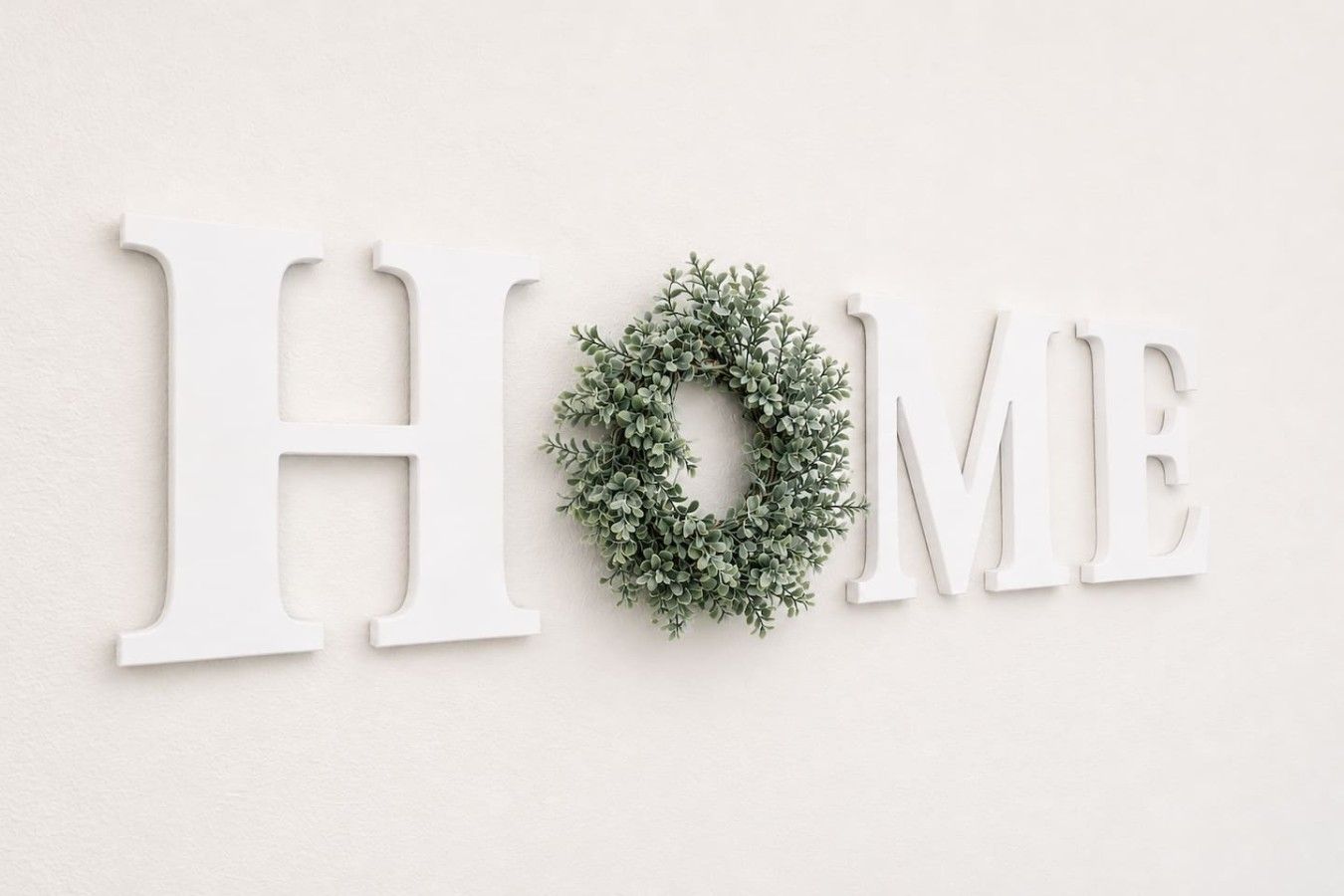 Een muur waarop het woord 'HOME' in grote witte letters staat, met een kleine groene krans tussen de letters 'O' en 'M'.