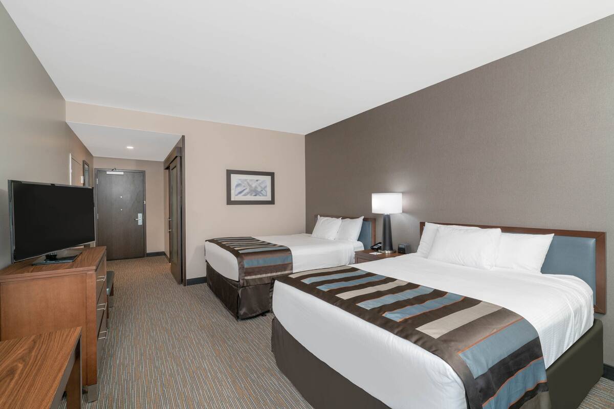 Ein Hotelzimmer mit einem großen Bett, einem kleineren Bett, einem Schreibtisch mit Fernseher und einer Tür zu einem weiteren Zimmer.