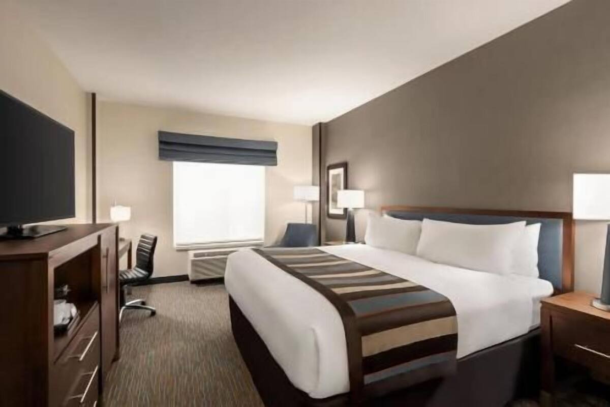Ein Hotelzimmer mit Bett, Schreibtisch, Stuhl, Fernseher und Fenster.