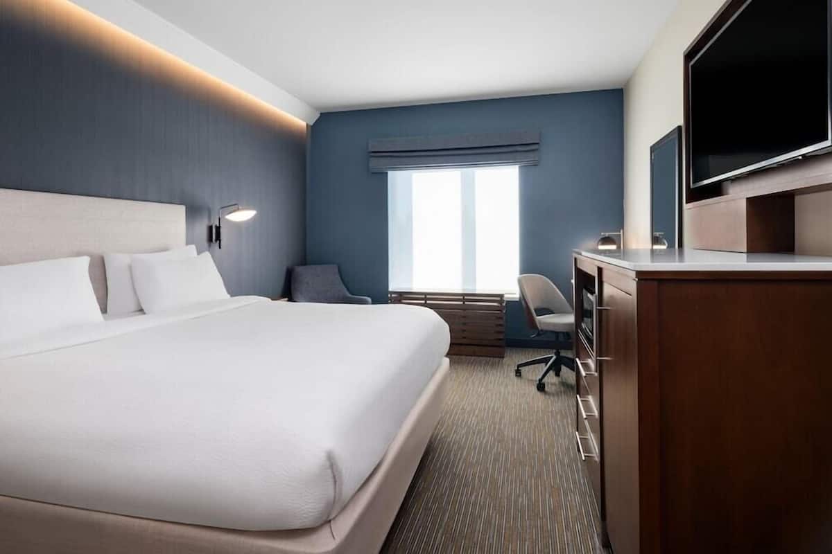 Ein Hotelzimmer mit einem großen Bett, einem Schreibtisch, einem Sessel, einem Fernseher und einem Fenster.