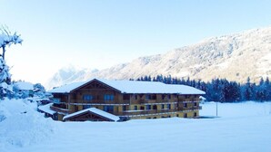Un chalet en bois à plusieurs étages, doté de balcons, entouré de montagnes et d’arbres couverts de neige.