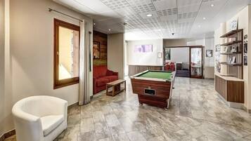 Um espaço moderno em ambiente interno com mesa de bilhar, um sofá vermelho e uma poltrona branca.