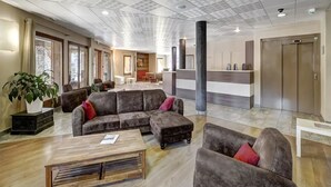 Un hall d’entrée spacieux, avec un grand canapé d’angle, une table basse en bois et un comptoir de réception.