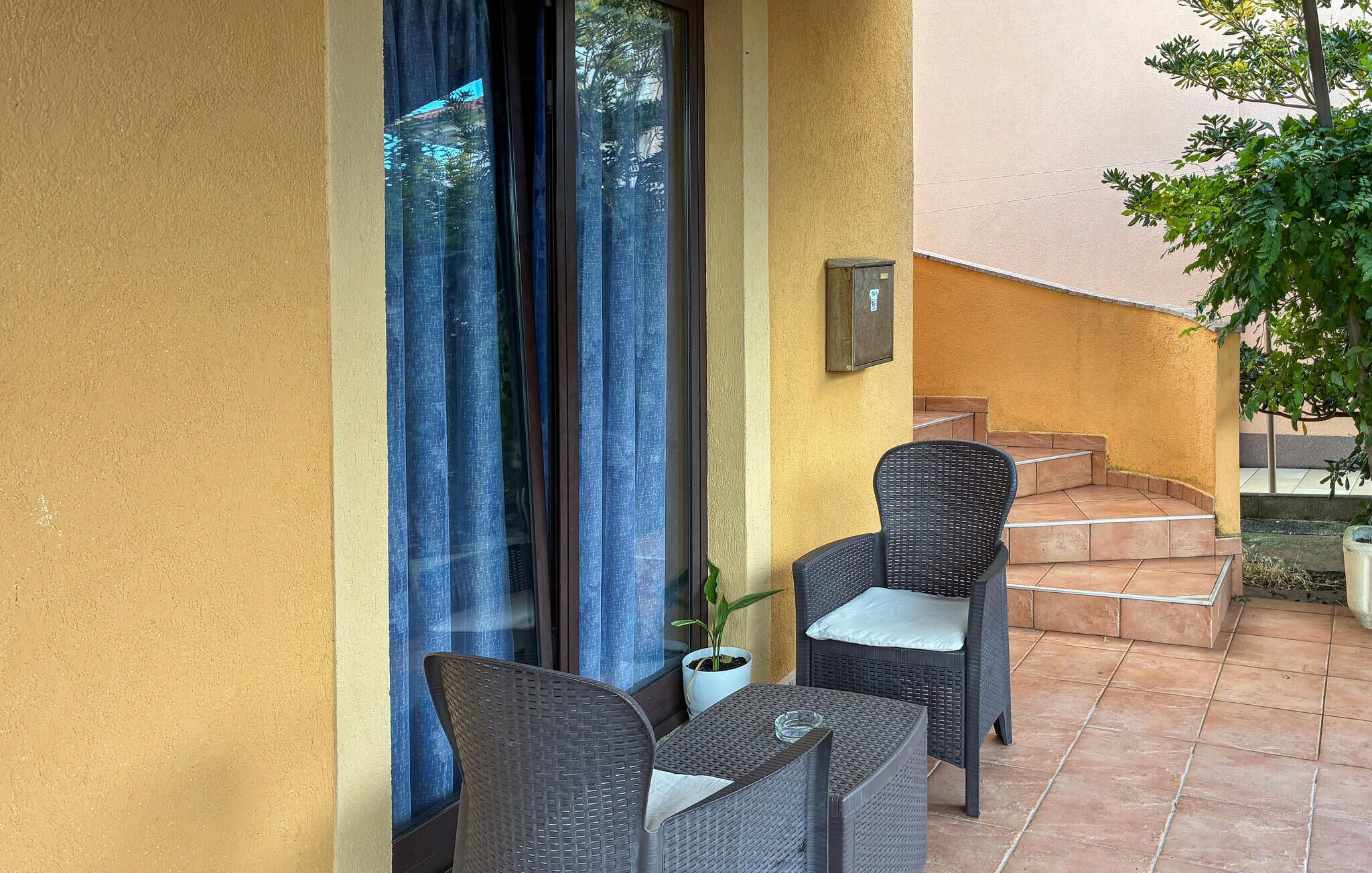 A small outdoor patio with wicker furniture and a potted plant.