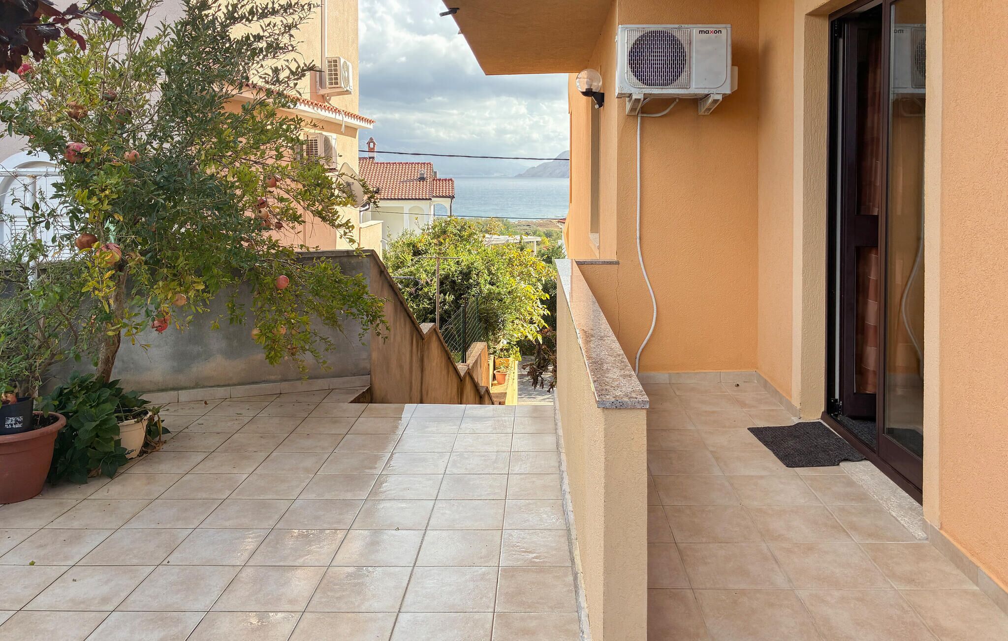 Un balcone con pavimento piastrellato, piante in vaso e vista sul mare.