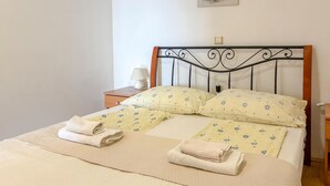 A neatly made bed with a quilted cover and two pillows, a bedside lamp, and a small bedside table with a lamp. - Nice apartment in Lopar with WiFi (Lopar)