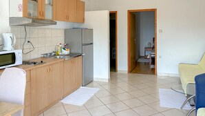 A compact kitchen with wooden cabinets, a microwave, and a refrigerator. There is a small dining area with a chair and a table. - Nice apartment in Lopar with WiFi (Lopar)