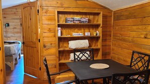 Ein gemütliches Zimmer mit Holzwänden, einem Bett, einem kleinen Tisch mit Stühlen und einem Bücherregal mit Büchern und Gegenständen.