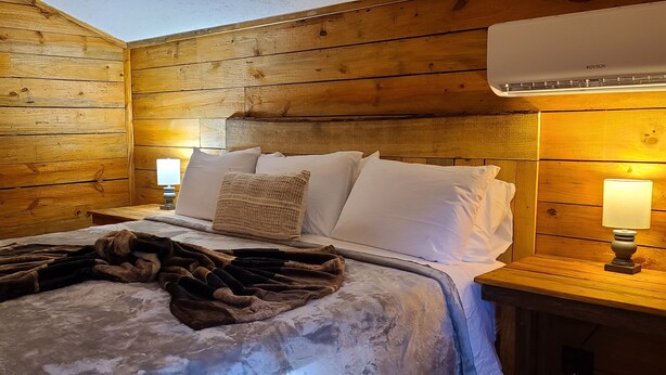Ein holzgetäfeltes Zimmer im Blockhausstil mit einem Bett, zwei Nachttischlampen und einer unter der Decke montierten Klimaanlage.