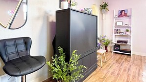 Un salón con un mueble de entretenimiento negro, una silla negra, una mesita de madera y una estantería con plantas.