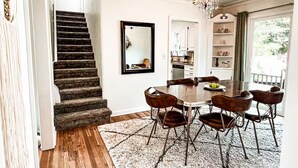 A dining area with a round table, six chairs, and a chandelier. A staircase leads to another room. - Amazing 3-Bed Cottage with Spa, Home Office & Gym (Idaho Falls)