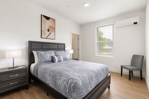 Een moderne slaapkamer met een bed, nachtkastjes, een stoel en een raam met zonwering.