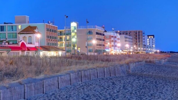 Ein Strandhotel mit mehreren Gebäuden, darunter ein markantes Gebäude mit rotem Dach, und einem Sandstrand.