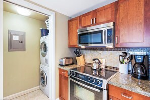 A compact kitchen with a washing machine, microwave, toaster, kettle, coffee maker, and a tiled backsplash. - Honua Kai | Ocean View 5 BR, Sleeps 18 | Car Incl. w/ 6+ Nights | HKH ML-1721 by KBM (Lahaina)