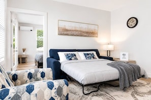 A bedroom with a bed, a nightstand, a wall clock, and a painting. - Elegant 2 Bed 2 Bath • Downtown • Free Parking (Hot Springs)