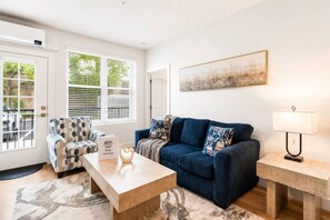 A modern living room with a blue sofa, a patterned armchair, a coffee table, and a lamp. - Elegant 2 Bed 2 Bath • Downtown • Free Parking (Hot Springs)