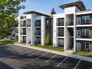 Un immeuble résidentiel à plusieurs étages, doté de balcons, d’un parking et surplombant un ciel dégagé.